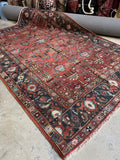 Antique Persian Heriz rug from early 1900s with terracotta red field and botanical motifs.