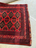 One end view of rug with red and navy pattern highlighting tribal artistry of Afghan weaving.