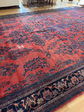 A large  12x22 traditional oriental area rug with a red field and dark blue floral motifs, laid out on a light wood floor in a room