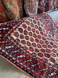 Ivory field antique tribal scatter rug with repeating red and navy paisley motifs.
