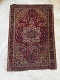 Overhead flat lay showing full pattern of 1930s antique Persian Sarouk rug with central medallion, red field, and floral chain border.