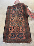 A rectangular vintage blush and coral Persian area rug laid flat on a concrete floor, featuring a dusty rose and dark brown base with navy blue and beige floral motifs.