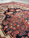 Antique Persian wool rug with ivory field, navy medallion, and floral border.