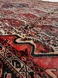 A close-up view of a small vintage Persian area rug with intricate woven details in red, beige, black, and navy blue.