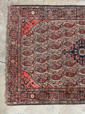 A traditional Persian area rug with a red and beige floral pattern, laid out on a light concrete floor.