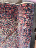 Corner view of antique Persian Kerman rug featuring a vibrant floral garden design on a creamy ivory ground.
