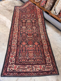 Antique Persian runner rug 4x9 laid flat on concrete, displaying a rich red, navy, and tan small-scale pattern.