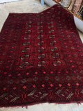 Full view of a dark, moody Afghani rug with repeating tribal medallions.