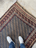Top corner of antique Baluch rug showing transition from hand-knotted pile field to flat weave kilim end, two weaving techniques in one rug