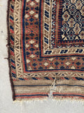 Corner of a patterned baluch rug with intricate designs on a navy background