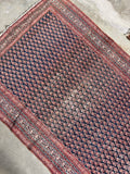 Angled view of antique Persian gallery rug showing all-over boteh paisley field with natural abrash color variation on deep navy ground