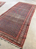 Second full view of antique Persian boteh rug showing gallery size proportion, midnight blue field and rust border from alternate angle