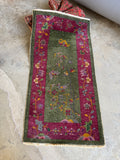 Antique botanical wool rug with butterflies, blossoms, and soft lavender accents against a green ground.