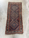 Skinny antique Baluchi hallway runner featuring ram’s horn tribal motifs and worn low wool pile.