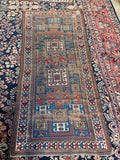 Worn antique Caucasian rug featuring distressed low pile and symbolic ram's horn motifs.