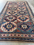 Antique vegetable dyed Kazak rug with ivory border and tribal symbolism.