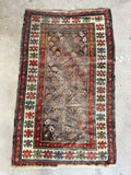 Antique Caucasian rug with a dark field filled with colorful paisley motifs and an ivory border.