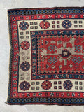 One end view of antique rug showing central field detail with geometric tribal forms on brick red ground.