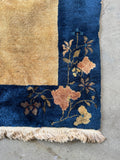 Corner view of velvety wool Art Deco area rug in wheat beige and navy blue palette.
