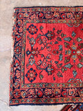 Hand knotted Persian wool rug in coral red with authentic edge wear and floral motif.
