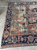 Antique Heriz rug with scattered wear and a navy border with tribal geometric pattern.