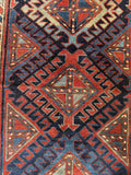 Close up of early 1900s Kazak rug with graphic tribal art and deep navy background.