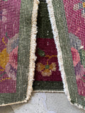 Underside view of antique Art Deco entry rug with a moss green center field and vivid pink floral border design.