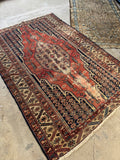 Antique Mazlaghan Persian rug with a red and navy lightning bolt medallion, laying flat on light gray concrete.