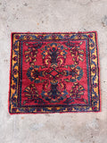Small Persian accent rug displayed on concrete showing intricate floral motif.