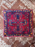 Small Persian rug mat displayed on concrete showing intricate floral pattern.