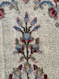 Close up of an antique Persian rug with botanical details against an ivory ground.