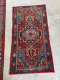 Hand knotted Persian Heriz rug. Small antique wool rug with brick red, navy, aqua blue, and camel tones in a bold tribal design.