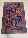 Jewel toned antique Persian rug with floral movement across the navy field.