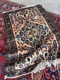 Antique Persian Lilihan small mat rug displaying an ivory field with delicate floral sprays laid on top of a larger carpet.