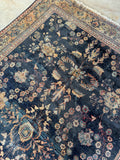 Worn Persian village rug with navy field and decorative botanical elements.