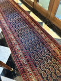 Time worn Persian hallway runner with low pile and scattered wear.