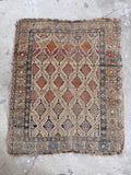 Antique tribal rug laid flat on concrete showing geometric tree motifs and warm wheat ground.