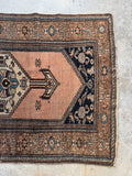 One end view of antique Persian rug featuring floral border and dark blue corners.