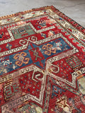 Antique tribal wool prayer rug with warm red field, geometric folk art motifs and authentic repairs.