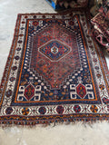 Border and field interaction on tribal Shiraz rug with navy and brick red tones.