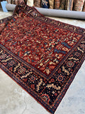 Antique Tabriz rug, angled view showing rich red field and navy border.