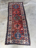 Handwoven wool runner with burnt sienna ground and symbolic motifs.