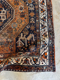 Corner view of worn antique Shiraz rug with intricate border work and peacock details.