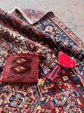 Hand woven Persian rug shot revealing tight weave construction and fringe detail with objects on top to display color depth.