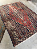 Circa 1910 antique Persian rug laid out next to another vintage textile on a neutral concrete floor.