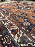 Antique tribal Shiraz rug with earthy tones, floral shrubs, and nomadic symbolism.