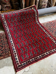 Small vintage Persian rug with bold red paisley motifs and ivory floral border.