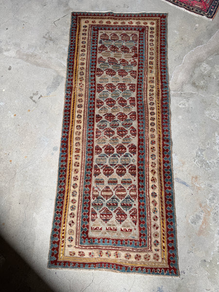 Full view of antique Caucasian runner with boteh motifs on a sandy ivory field.