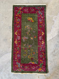 Small antique green and pink rug with low pile and flowering vine designs throughout.