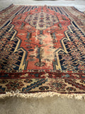 Vintage Persian rug showing worn fringe edges and intricate geometric hand-knotted weaving.
